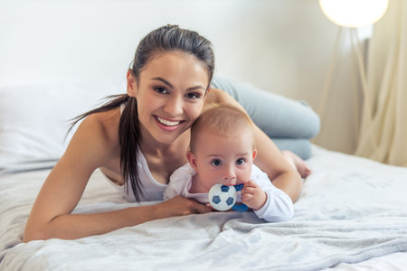 Portrait of beautiful young mom and her sweet little baby looking at camera and smiling, lying on...