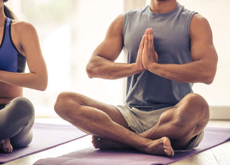 Cropped image of beautiful Afro American couple in sports clothes meditating in lotus position on mat while doing yogaの写真素材