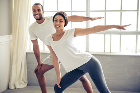 Beautiful Afro American couple is looking at camera and smiling while doing yoga at home