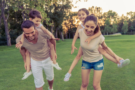 Beautiful happy family is smiling while having fun outdoors, kids are sitting pickaback