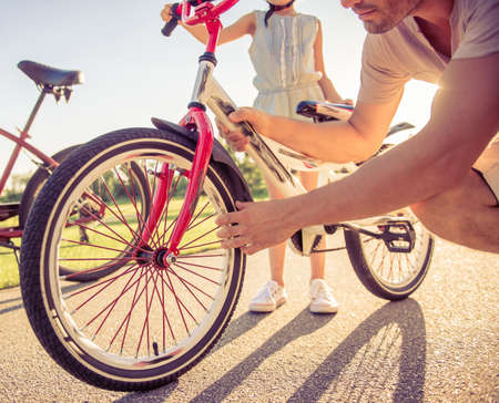 Cropped image of father checking wheel of her daughter's bicycle while they are riding bikes in parkの写真素材