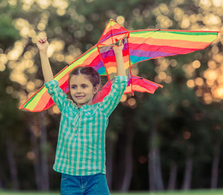 Beautiful little girl is holding a kite and smiling while playing outdoorsの写真素材