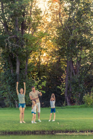 Full length image of happy family having fun while catching fish using a fishing rod in the pond in parkの写真素材