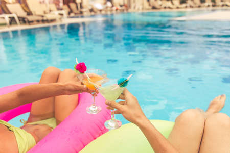Cropped image of beautiful girls in swimwear drinking cocktails while lying on swim rings in the poolの写真素材