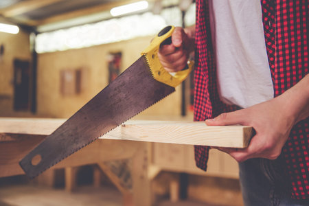 Cropped image of handsome carpenter cutting wood using a saw in the workshop