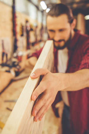 Handsome carpenter is measuring wood and smiling while working in the workshop. Hand in focusの写真素材