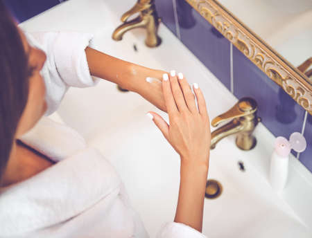 Cropped image of beautiful young woman in bathrobe using hand cream in the bathroomの写真素材