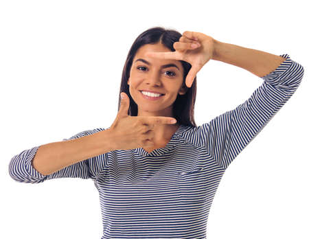 Beautiful young girl in casual clothes is making hand frame, looking at camera and smiling, isolated on whiteの写真素材