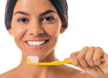 Portrait of beautiful girl with bare shoulders holding a toothbrush with toothpaste, looking at...
