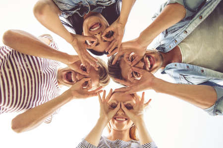Bottom view of beautiful stylish friends making glasses of fingers, looking at camera and smilingの写真素材