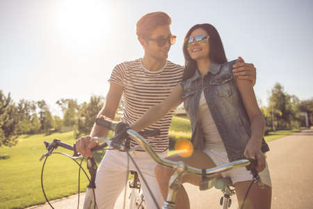 Beautiful couple is hugging, talking and smiling while cycling in the parkの写真素材