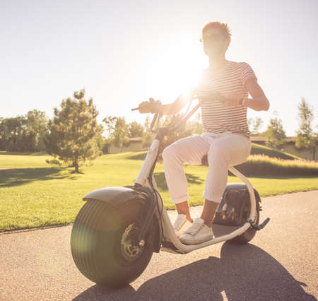 Handsome stylish man is smiling while riding on the electric scooter in the parkの写真素材