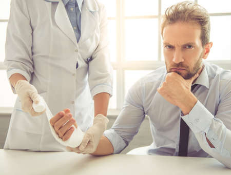 Cropped image of female doctor bandaging man's injured hand while working in her officeの写真素材