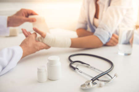 Cropped image of doctor bandaging woman's damaged hand while working in his officeの写真素材