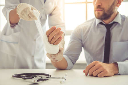 Cropped image of female doctor bandaging man's injured hand while working in her officeの写真素材