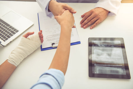 Cropped image of handsome medical doctor shaking hands with female patient while working in his officeの写真素材