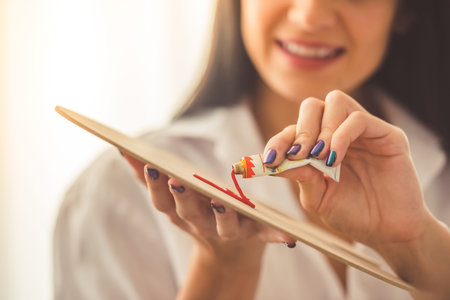Cropped image of attractive young female artist applying oil paint on the palette and smiling while working in her studioの写真素材