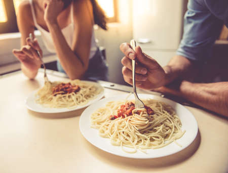 Cropped image of beautiful young couple eating spaghetti in kitchen at homeの写真素材