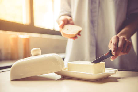 Cropped image of beautiful young girl making a toast with butter in kitchen at homeの写真素材