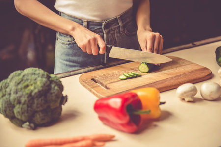 Cropped image of beautiful young girl cutting vegetables while cooking in kitchen at homeの写真素材