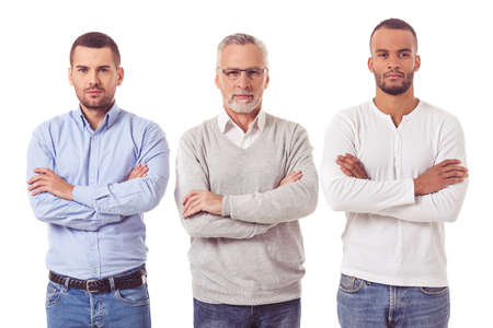 Three handsome businessmen in smart casual wear are looking at camera while standing with folded arms on a white backgroundの写真素材