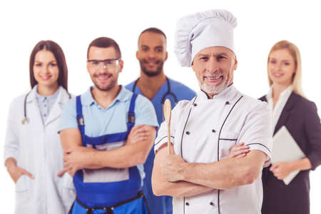 Beautiful people of different professions in uniforms are looking at camera and smiling, isolated on white. Handsome mature cook in the foregroundの写真素材