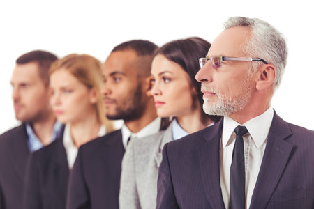 Beautiful business people in suits are standing one by one, handsome mature businessman in the foreground, isolated on a whiteの写真素材
