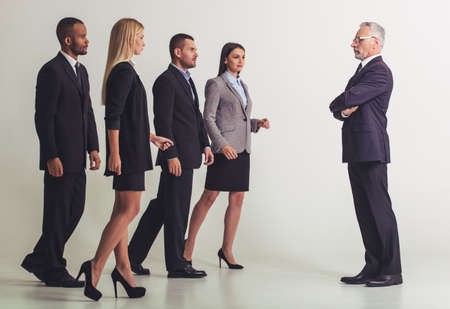 Full length portrait of mature boss standing with crossed arms and looking at his young business team, on a gray backgroundの写真素材