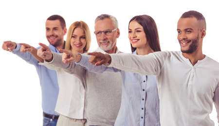 Beautiful business people in smart casual wear are pointing away and smiling while standing one by one, isolated on whiteの写真素材