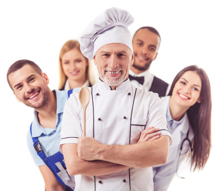 Beautiful people of different professions in uniforms are looking at camera and smiling, isolated on white. Handsome mature cook in the foregroundの写真素材