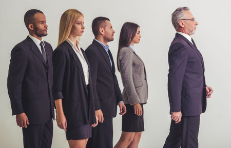 Beautiful business team is standing behind their handsome mature boss, on a gray backgroundの写真素材