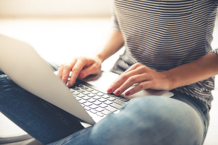 Cropped image of beautiful girl in casual clothes using a laptop while sitting on the floor at home
