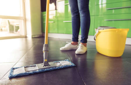 Cropped image of beautiful young woman using a mop while cleaning the floor in kitchenの写真素材