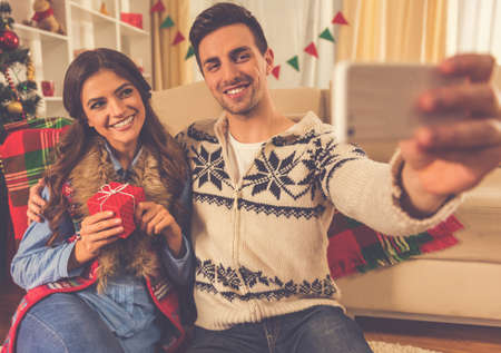 Happy young couple doing selfie using a smart phone and smiling while celebrating Christmas at homeの写真素材