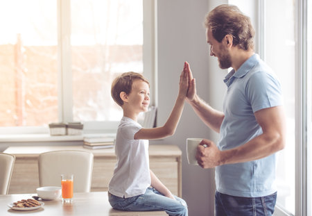 Father and son are giving high five and smiling while having a snack in kitchen