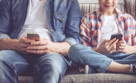 Cropped image of father and son using smartphones while spending time together at homeの写真素材