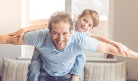 Father and son are smiling while spending time together. Little boy is sitting pickaback while...