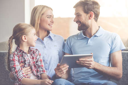 Beautiful young parents and their cute little daughter are using a digital tablet and smiling while spending time togetherの写真素材