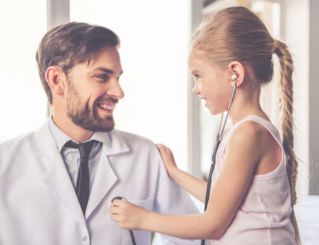 Cute little girl is examining handsome doctor using a stethoscope and smilingの写真素材