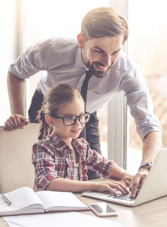 Handsome businessman and his cute little daughter are using a laptop and smiling while spending time togetherの写真素材