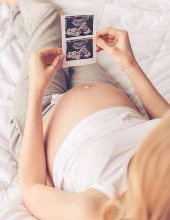 Cropped image of beautiful pregnant woman holding a sonogram while sitting on bedの写真素材