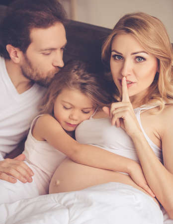 Beautiful pregnant woman, her handsome husband and cute daughter are spending time together in bed. Little girl is asleepの写真素材