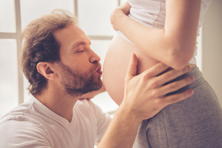 Handsome man is kissing his beautiful pregnant wife's tummy