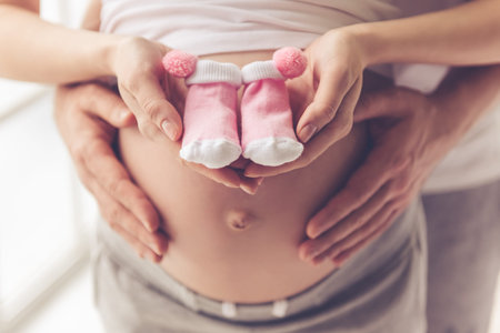 Cropped image of beautiful pregnant woman and her handsome husband holding baby shoes and hugging...