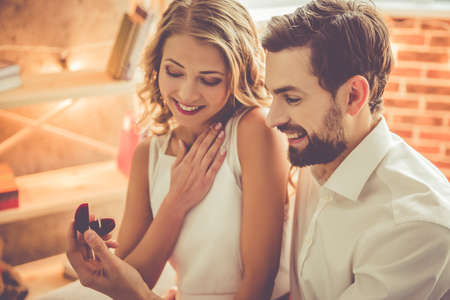 Handsome elegant guy is proposing to his beautiful girlfriend and smiling while they having a romantic date at homeの写真素材