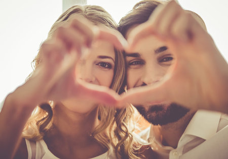 Beautiful young couple is making heart of fingers and smiling while celebrating at home