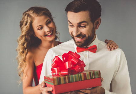 Beautiful elegant girl is presenting a gift to her handsome boyfriend and smiling