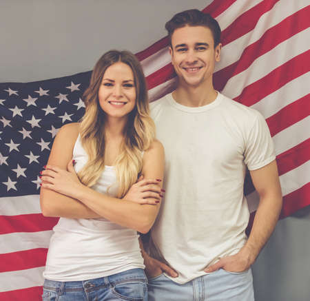 Beautiful young couple is looking at camera and smiling, on American flag backgroundの写真素材