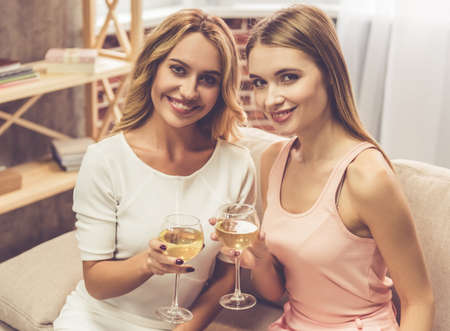 Beautiful girls in dresses are holding glasses of champagne, looking at camera and smiling during a partyの写真素材