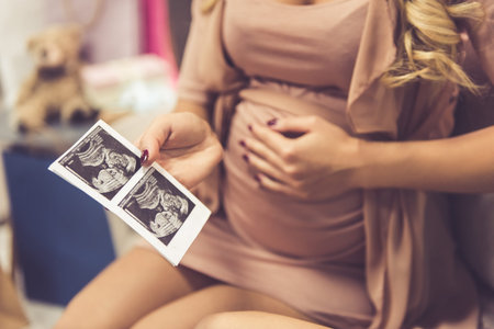 Cropped image of beautiful pregnant woman holding a sonogram while sitting on couch at home